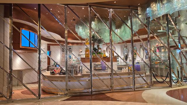 Large glass-encased chocolate fountain with white, milk, and dark chocolate streams circulating through overhead pipes.