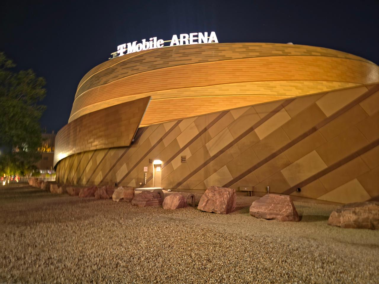 The glass and copper-colored exterior of T-Mobile Arena overlooking an open pedestrian plaza on the Las Vegas Strip.